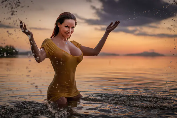Bianca Beauchamp in a gold dress, splashing through the water at sunset