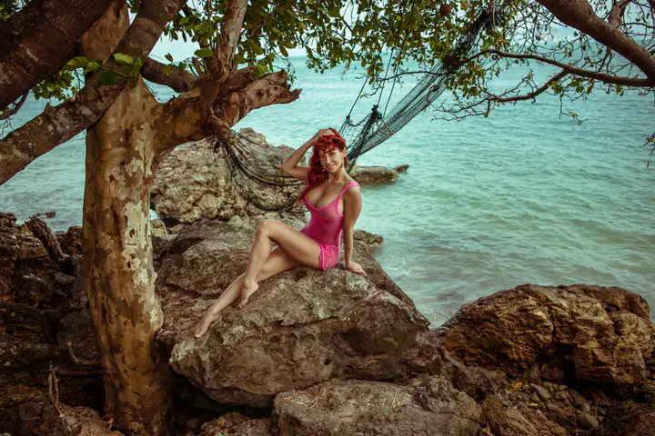 Bianca Beauchamp seated on rocks by the sea, under an overhanging tree